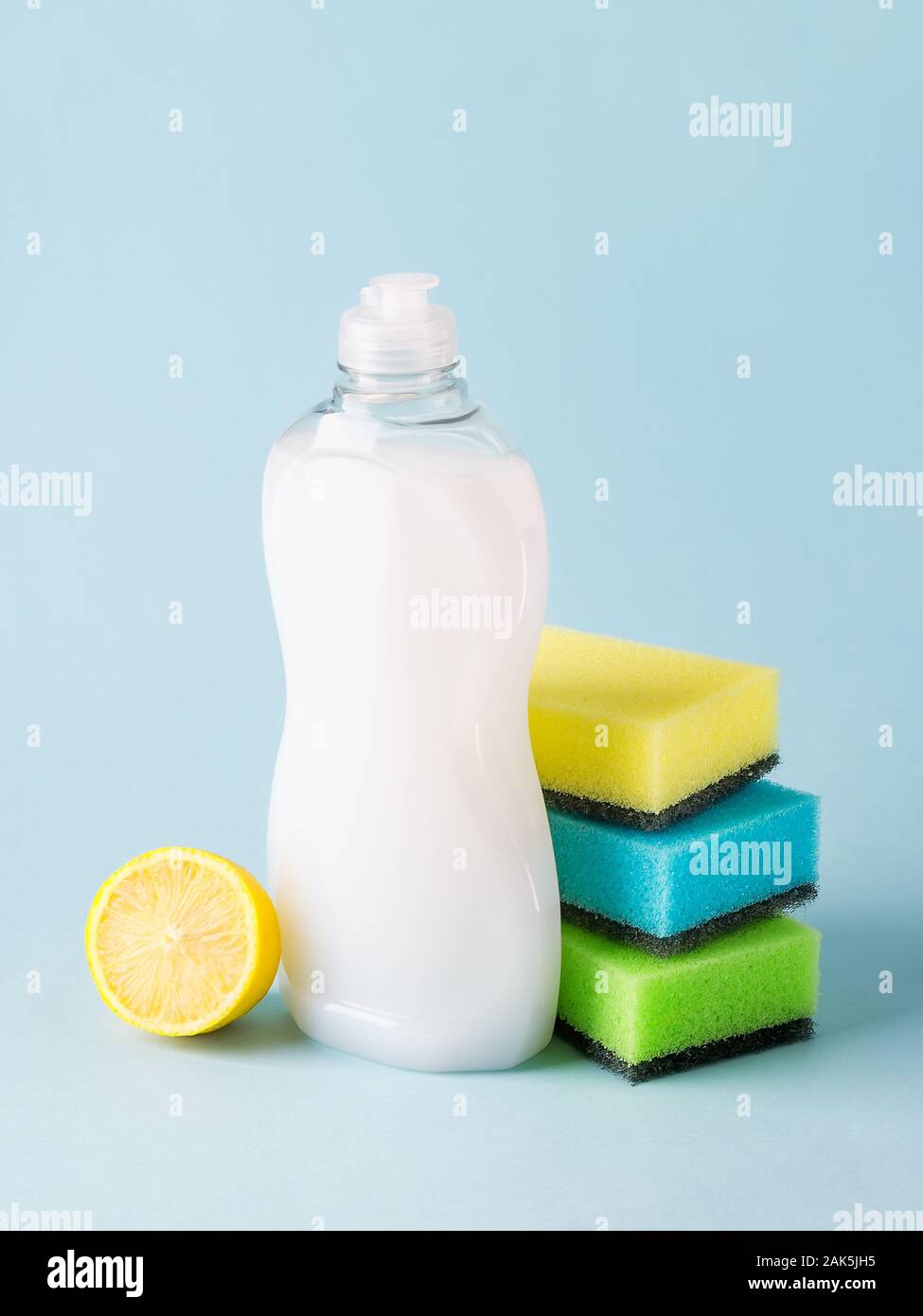 Liquide vaisselle blanche dans une bouteille en plastique, mousse de citron et trois éponges. Pureté et produits chimiques ménagers. Cuisine détergent sur un bleu pastel. Banque D'Images
