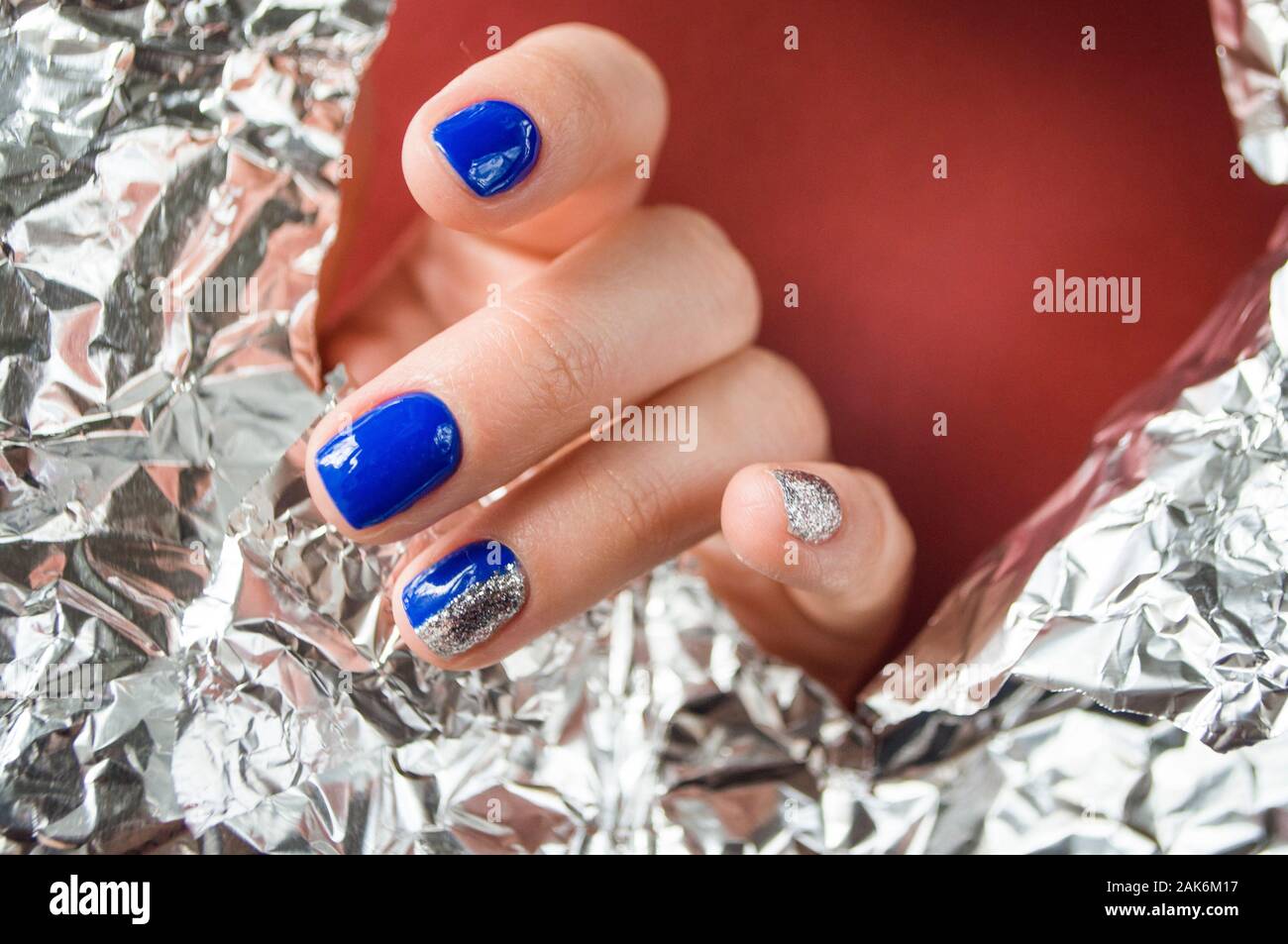 La main de la jeune femme avec une belle manucure bleu sur fond rouge avec du papier brillant métallique. Couleur 2020 tendance. Banque D'Images
