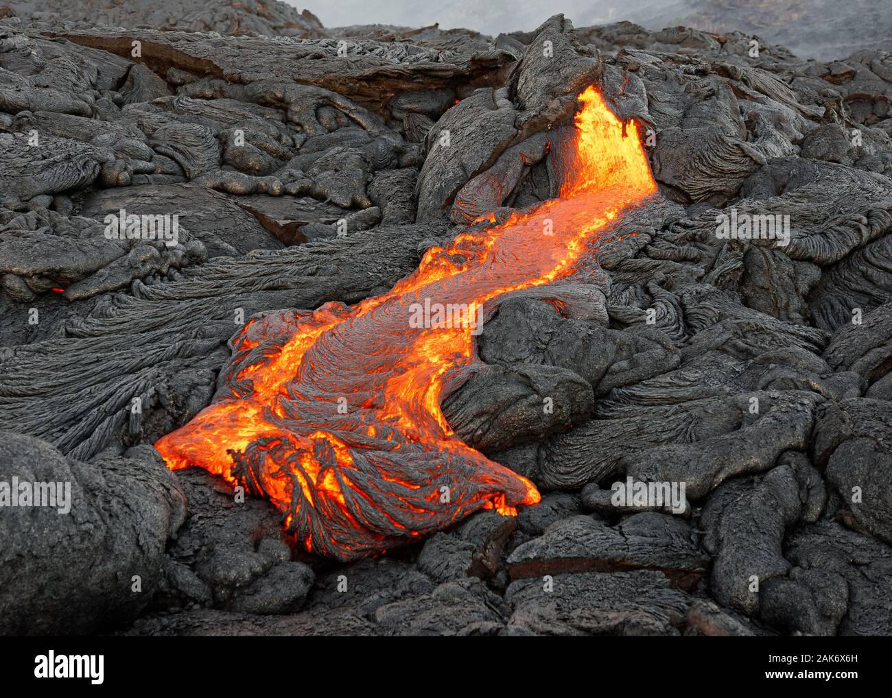 D'un magma chaud active lava flow émerge d'une fissure, la chaleur de la lave incandescente rend l'air vibrer, la lave se refroidit et se solidifie lentement Banque D'Images