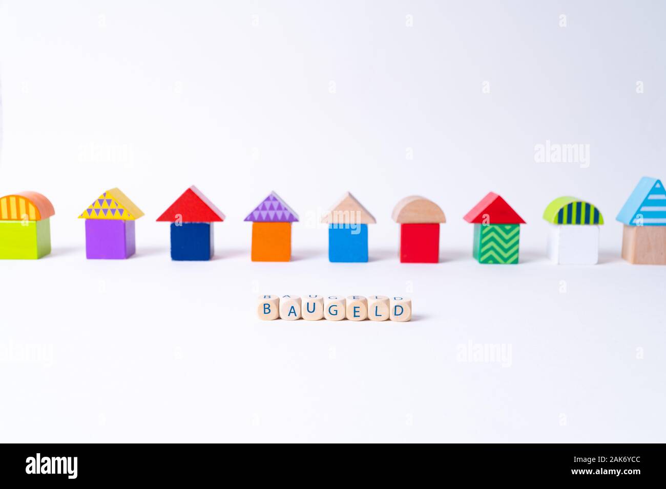 Glaçons avec des lettres pour dire 'Baugeld', le mot allemand pour de l'argent pour construire une maison en face d'une rangée de maisons construites de blocs de jouets Jouets colorés Banque D'Images