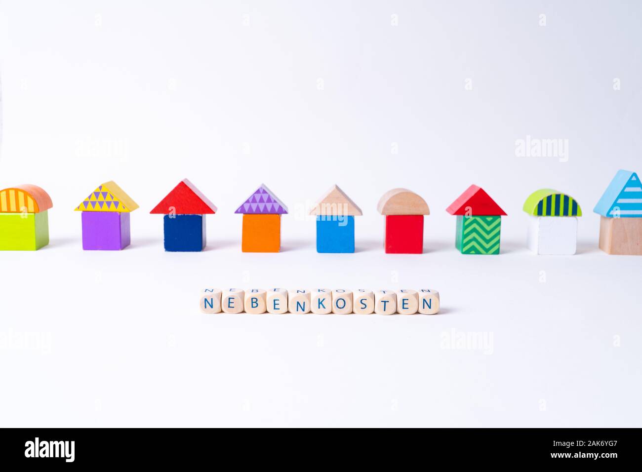 Glaçons avec des lettres pour dire 'Nebenkosten', le mot allemand pour les coûts supplémentaires en face d'une rangée de maisons construites de blocs de jouets Jouets colorés Banque D'Images