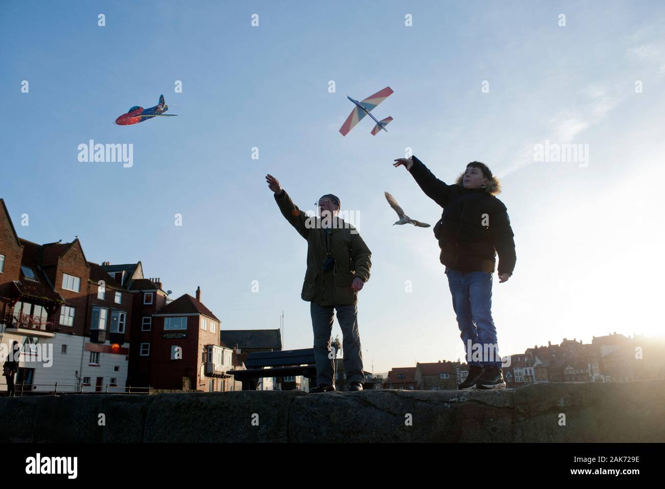 83 ans, grand-père et petit-fils d'adolescent flying paper planes ensemble off Tate Hill pier à Whitby, North Yorkshire, UK. Banque D'Images