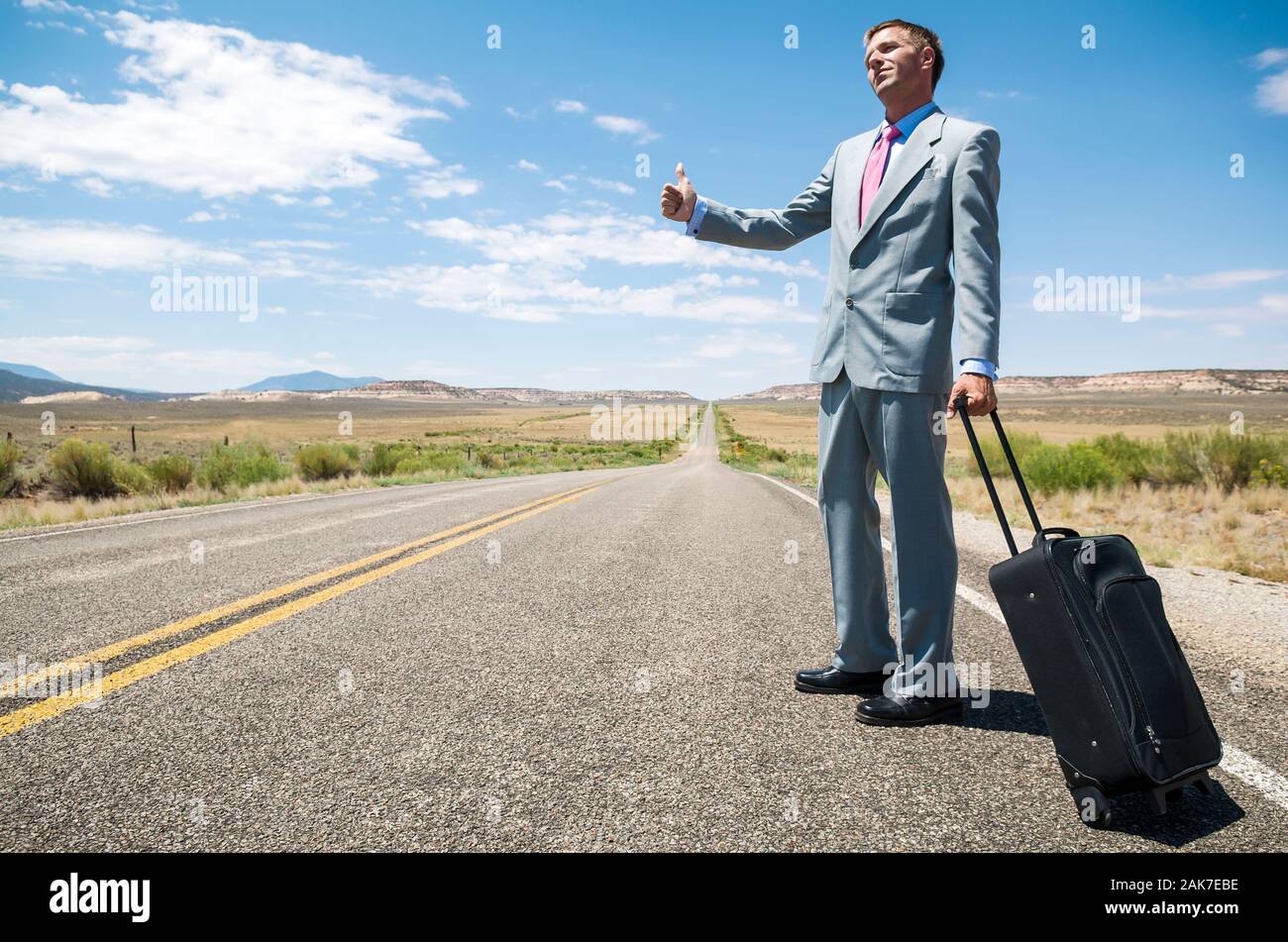 Stranded man avec sa valise roulant l'attelage d'une balade sur un tronçon de route solitaire Banque D'Images