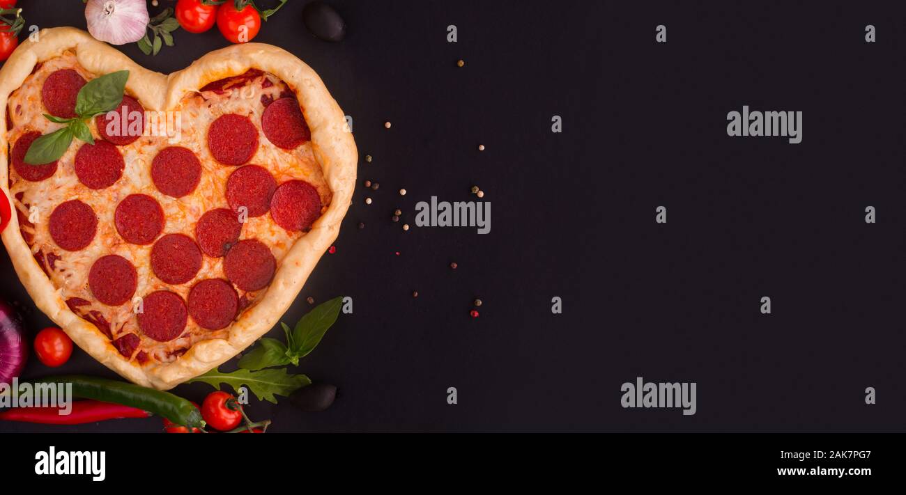En forme de coeur avec pepperoni pizza avec des ingrédients sur fond noir. Concept de l'amour romantique pour la Saint-valentin . Aime la nourriture Banque D'Images