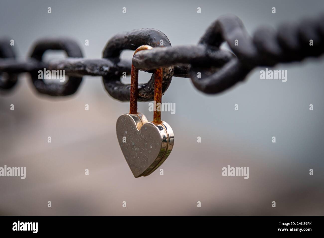 Un romantique et fermée en forme de coeur rouillé suspendu à un cadenas à côté d'une chaîne avec la rivière paysage flou en arrière-plan. Concept de longue durée Banque D'Images