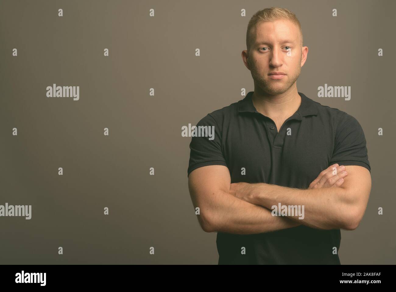 L'homme aux cheveux blonds portant polo noir à l'arrière-plan gris Banque D'Images