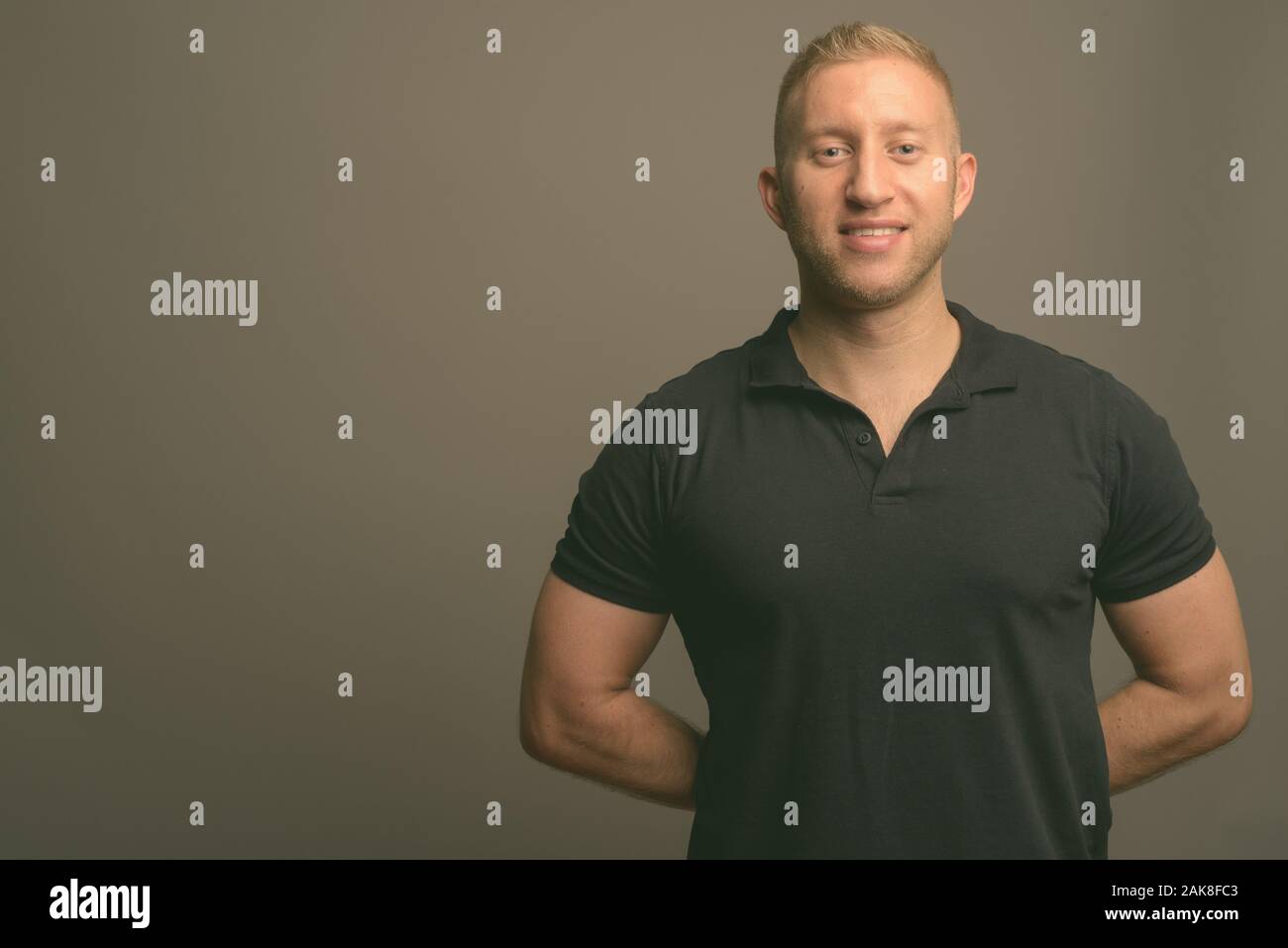 L'homme aux cheveux blonds portant polo noir à l'arrière-plan gris Banque D'Images