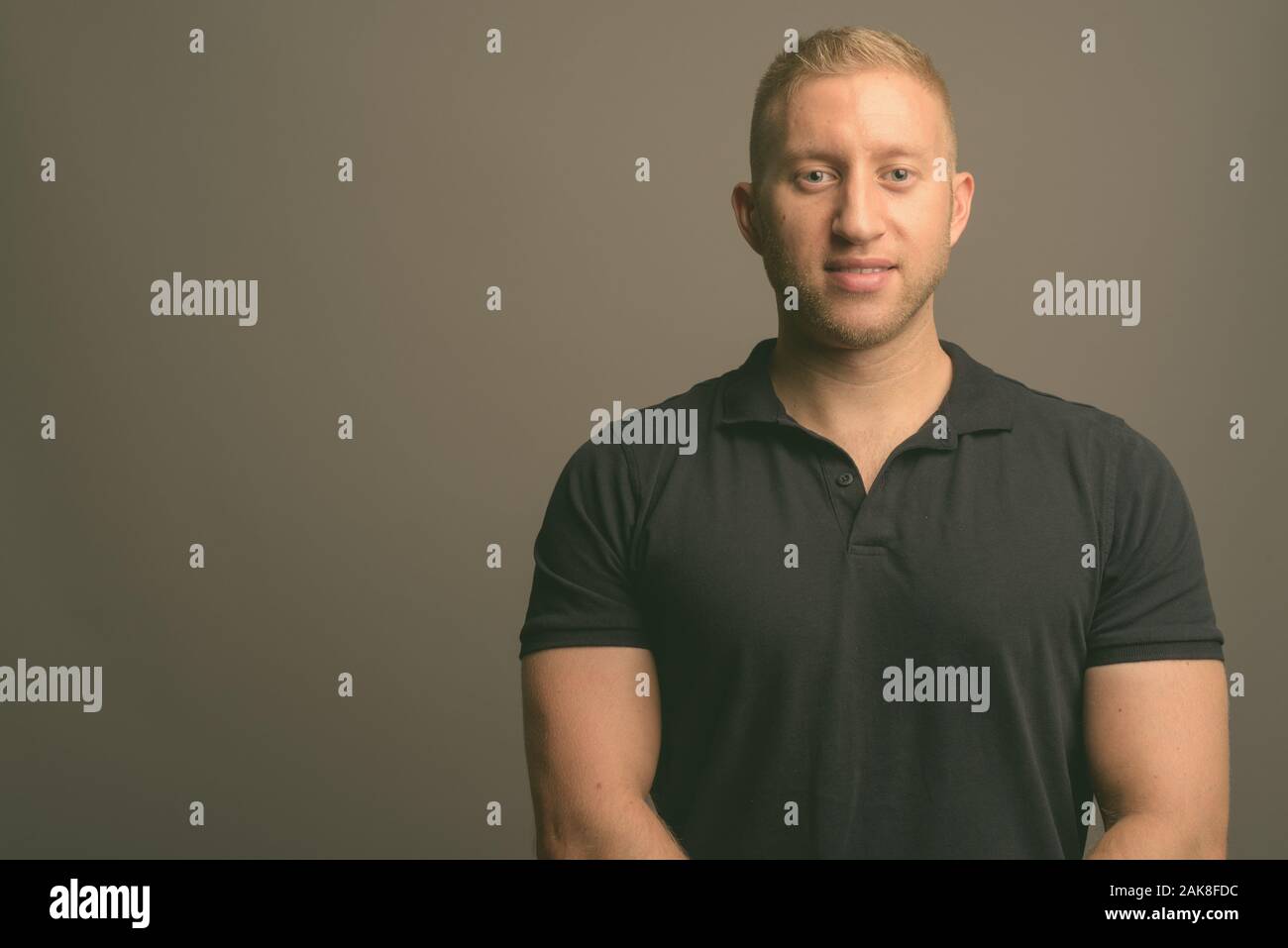 L'homme aux cheveux blonds portant polo noir à l'arrière-plan gris Banque D'Images