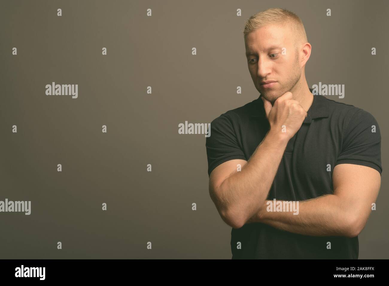 L'homme aux cheveux blonds portant polo noir à l'arrière-plan gris Banque D'Images