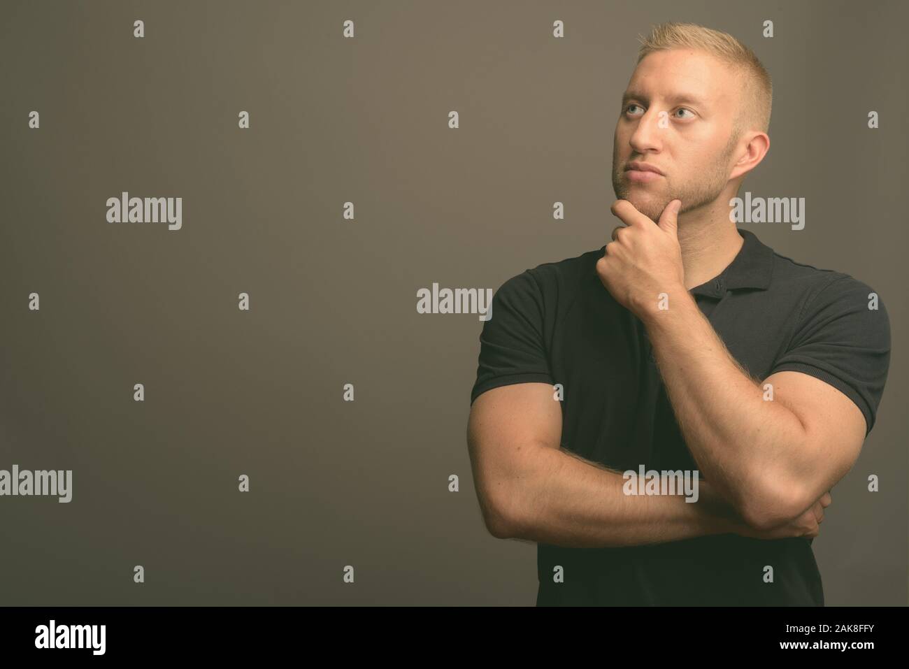 L'homme aux cheveux blonds portant polo noir à l'arrière-plan gris Banque D'Images