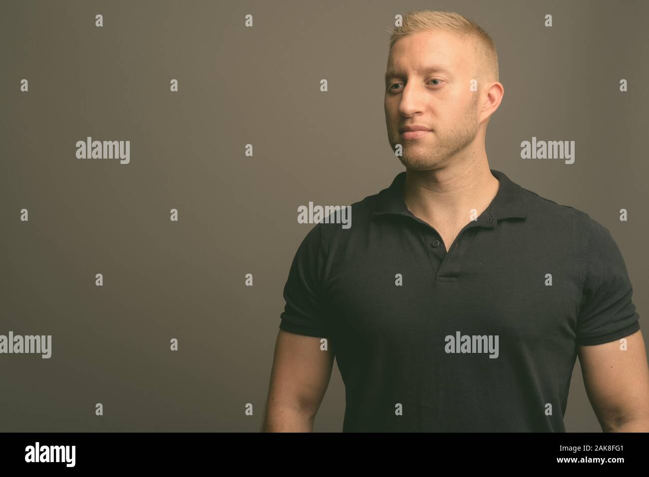 L'homme aux cheveux blonds portant polo noir à l'arrière-plan gris Banque D'Images