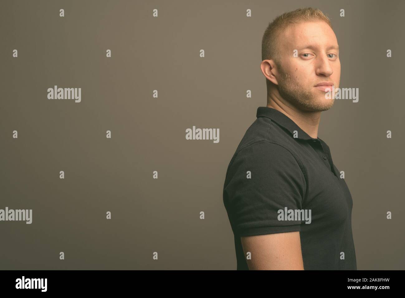 L'homme aux cheveux blonds portant polo noir à l'arrière-plan gris Banque D'Images