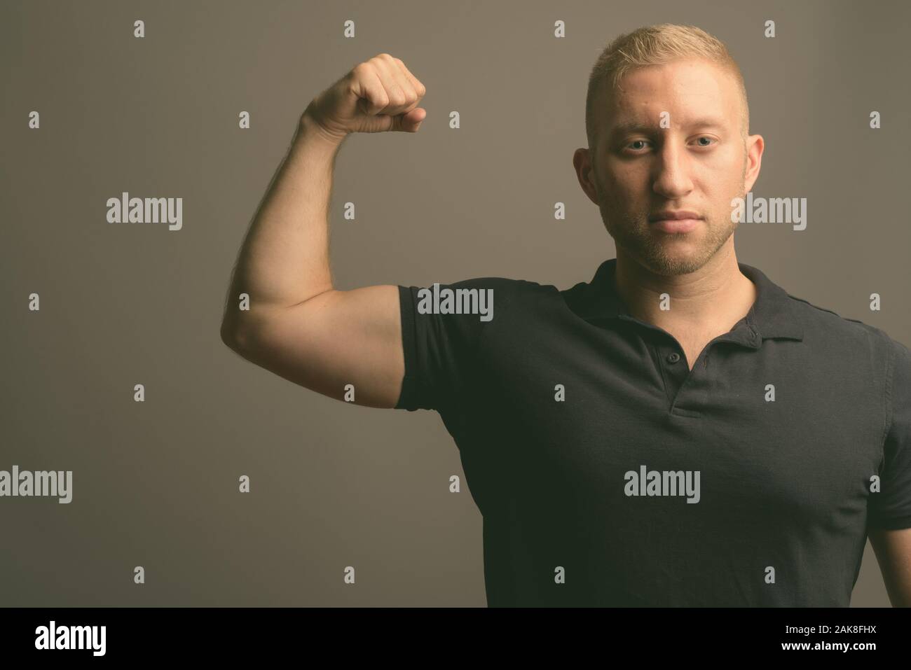 L'homme aux cheveux blonds portant polo noir à l'arrière-plan gris Banque D'Images