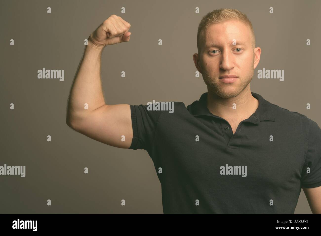 L'homme aux cheveux blonds portant polo noir à l'arrière-plan gris Banque D'Images