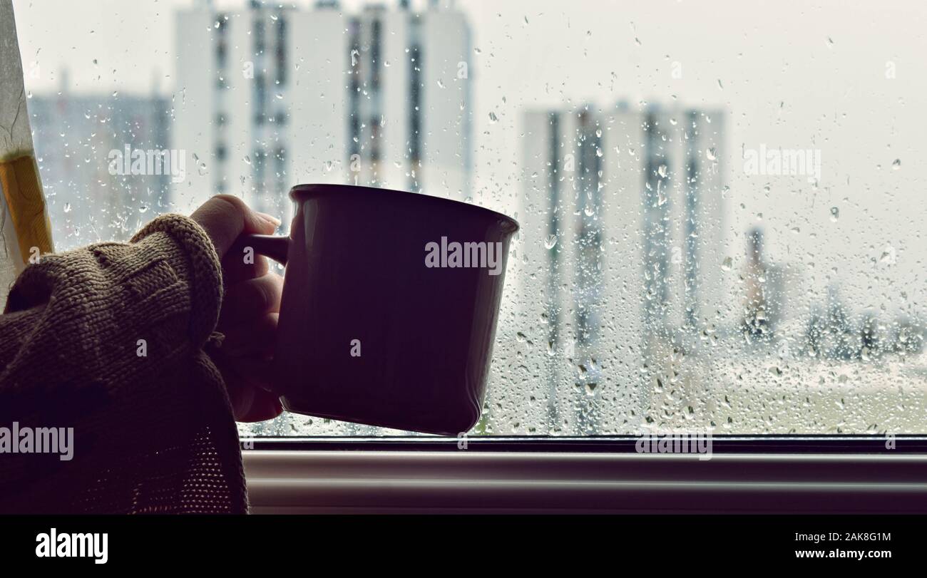 Femme Hand holding tasse de café chaud ou un thé dans la lumière du soleil du matin sur un fond de fenêtre humide avec des gouttes de confort / Pause café Banque D'Images