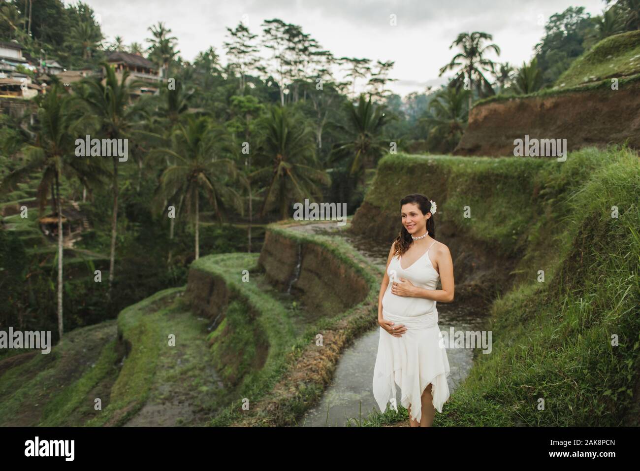Jeune femme enceinte en robe blanche avec vue sur les rizières en terrasses  de Bali dans la lumière du soleil du matin. Harmonie avec la nature.  Concept de la grossesse Photo Stock -