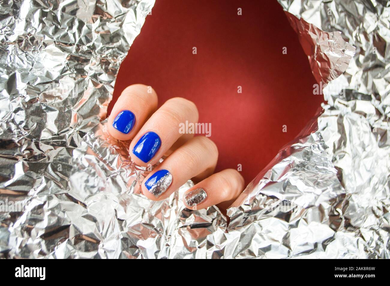La main de la jeune femme avec une belle manucure bleu sur fond rouge avec du papier brillant métallique. Couleur 2020 tendance. Banque D'Images