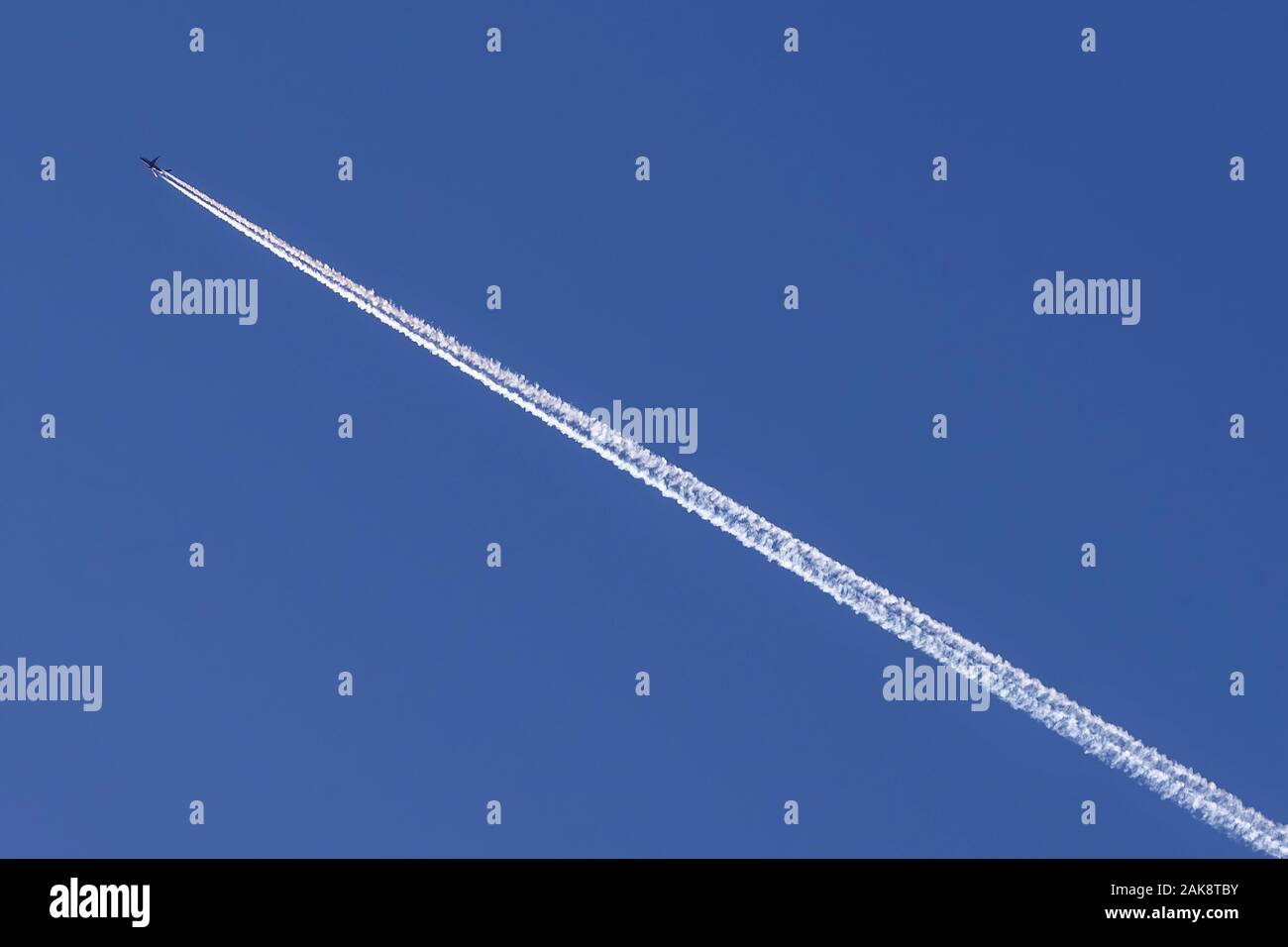 Un avion traverse le ciel bleu en diagonale, laissant derrière eux une longue piste blanche Banque D'Images
