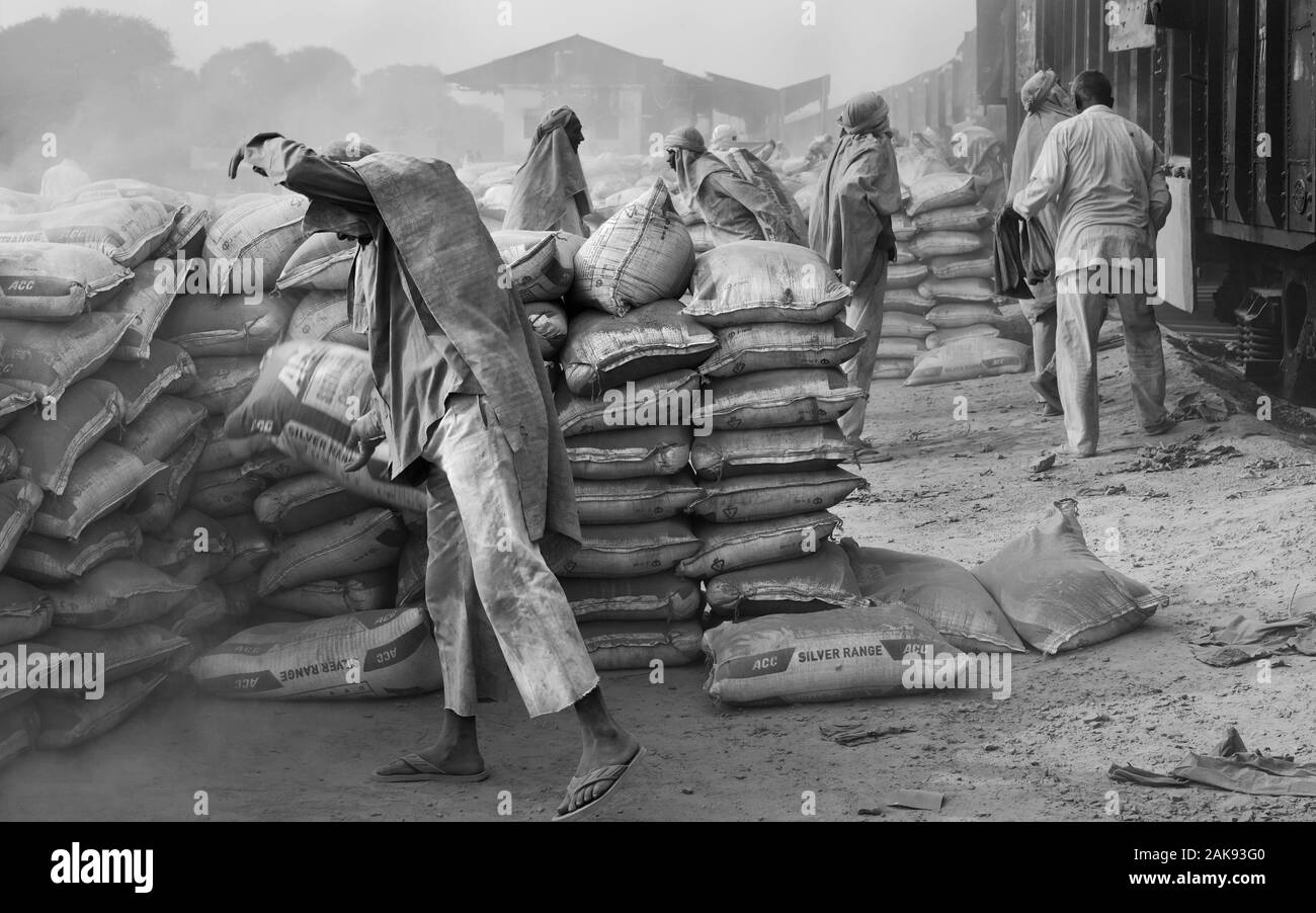 Équipe de travailleurs masculins dans des conditions poussiéreuses déplacer de gros sacs de ciment d'entraîner dans des conditions chaudes de l'été à Mathura, Uttar Pradesh, Inde. Banque D'Images