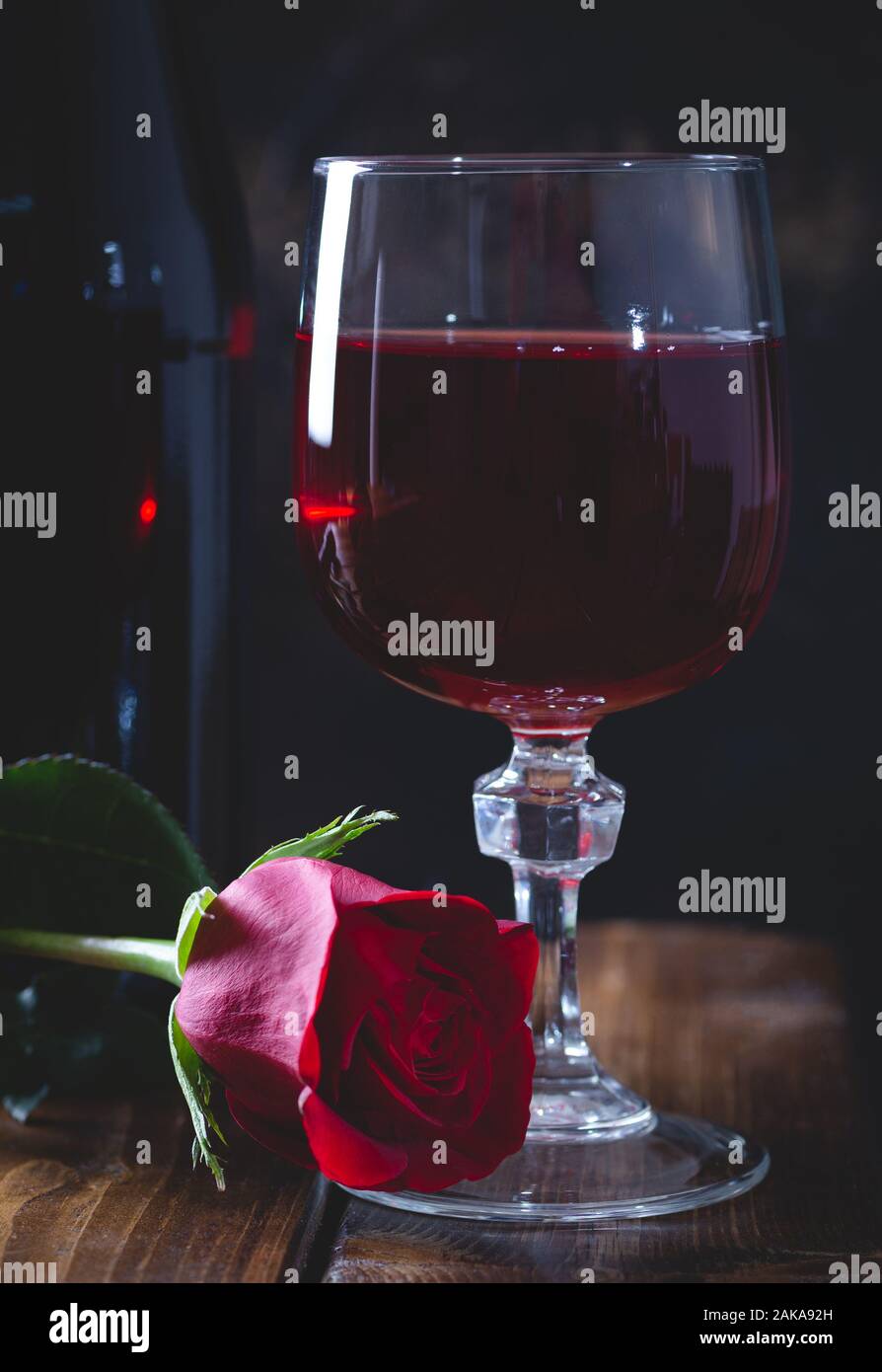 Dark définition d'un verre de vin et une rose rouge avec une bouteille en arrière-plan sur une table en bois Banque D'Images