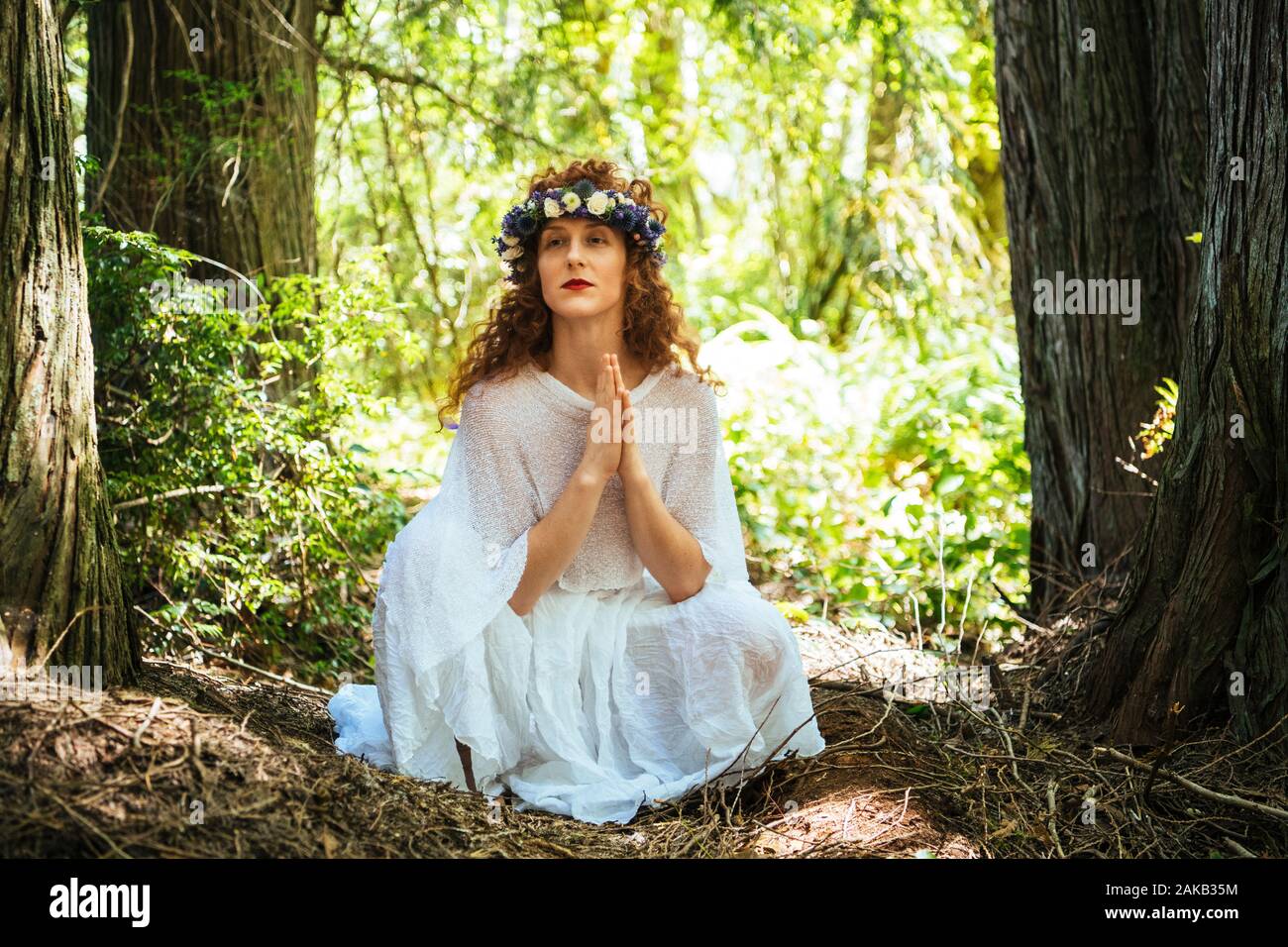 Femme avec des fleurs assis avec les mains jointes en forêt, Bainbridge Island, Washington State, USA Banque D'Images