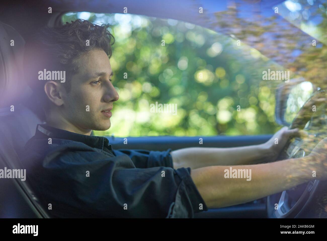 Jeune conducteur avec les mains à la roue, verdure en arrière-plan Banque D'Images