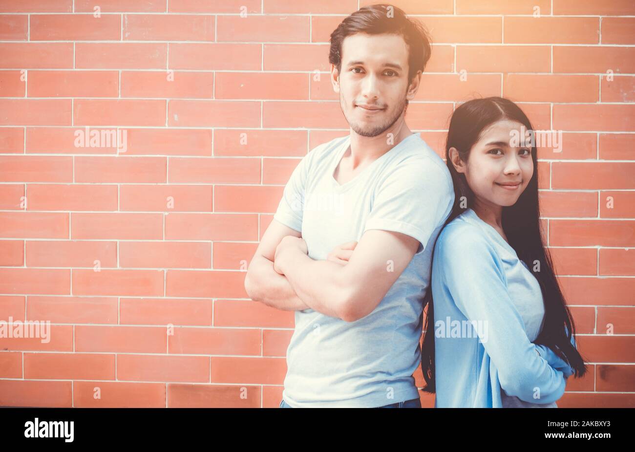 Jeune couple homme et femme asiatique bras croisés et stand attrayant sourire tout en dos à dos sur mur de brique avec fond romantique, petit ami et girl Banque D'Images