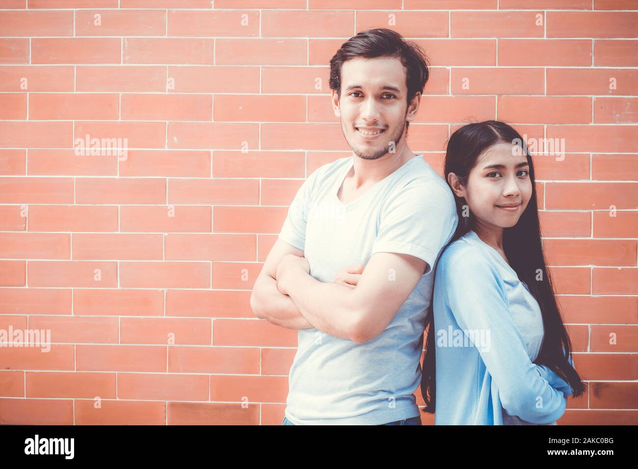 Jeune couple homme et femme asiatique bras croisés et stand attrayant sourire tout en dos à dos sur mur de brique avec fond romantique, petit ami et girl Banque D'Images