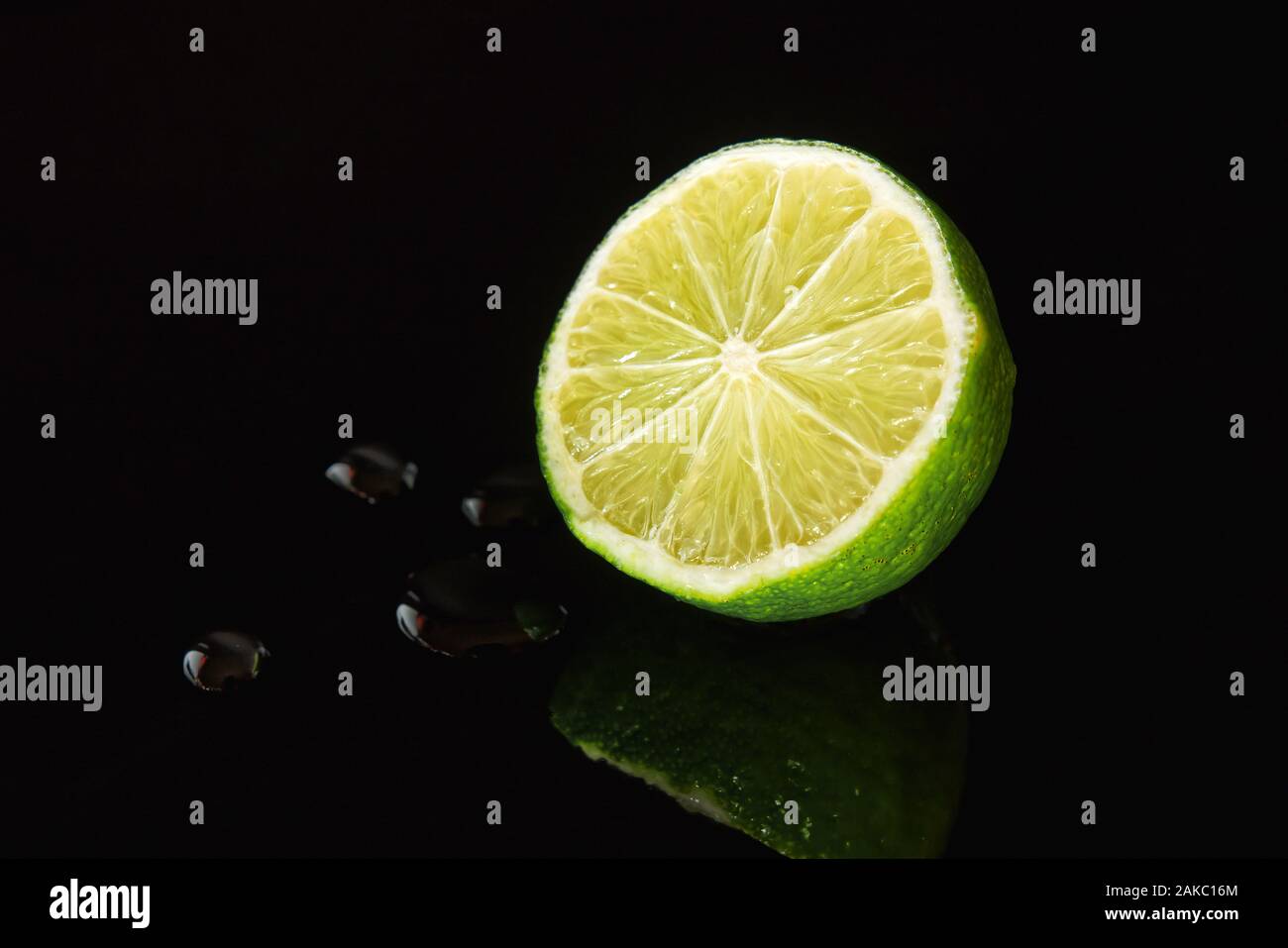 Demi-citron sur la surface noir brillant avec quelques gouttes et réflexions Banque D'Images