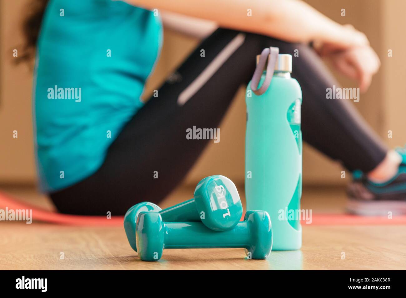 Stock photo de deux haltères et une bouteille. Dans l'arrière-plan une jeune femme se reposant après l'exercice Banque D'Images
