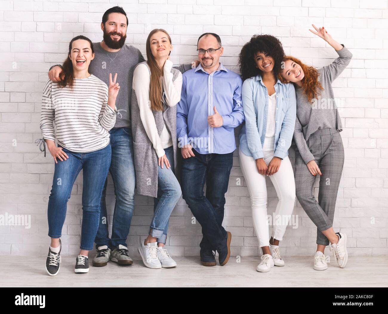 Une vraie amitié. Groupe de gens sympathiques embrassant ensemble, white brick wall background Banque D'Images