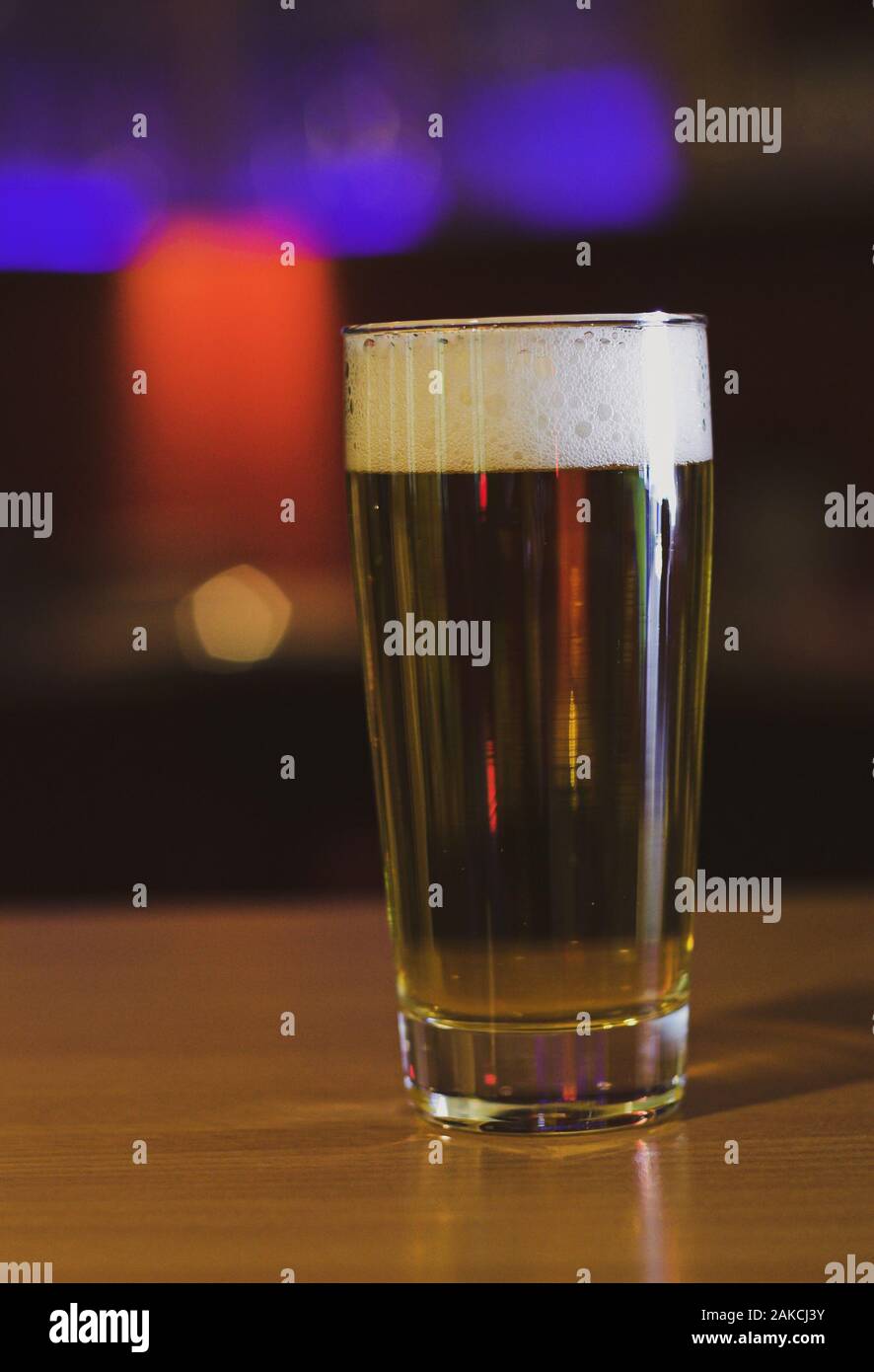 Un verre de bière pression sur un comptoir en bois poli avec les effets de lumière en arrière-plan dans une atmosphère de pub Banque D'Images