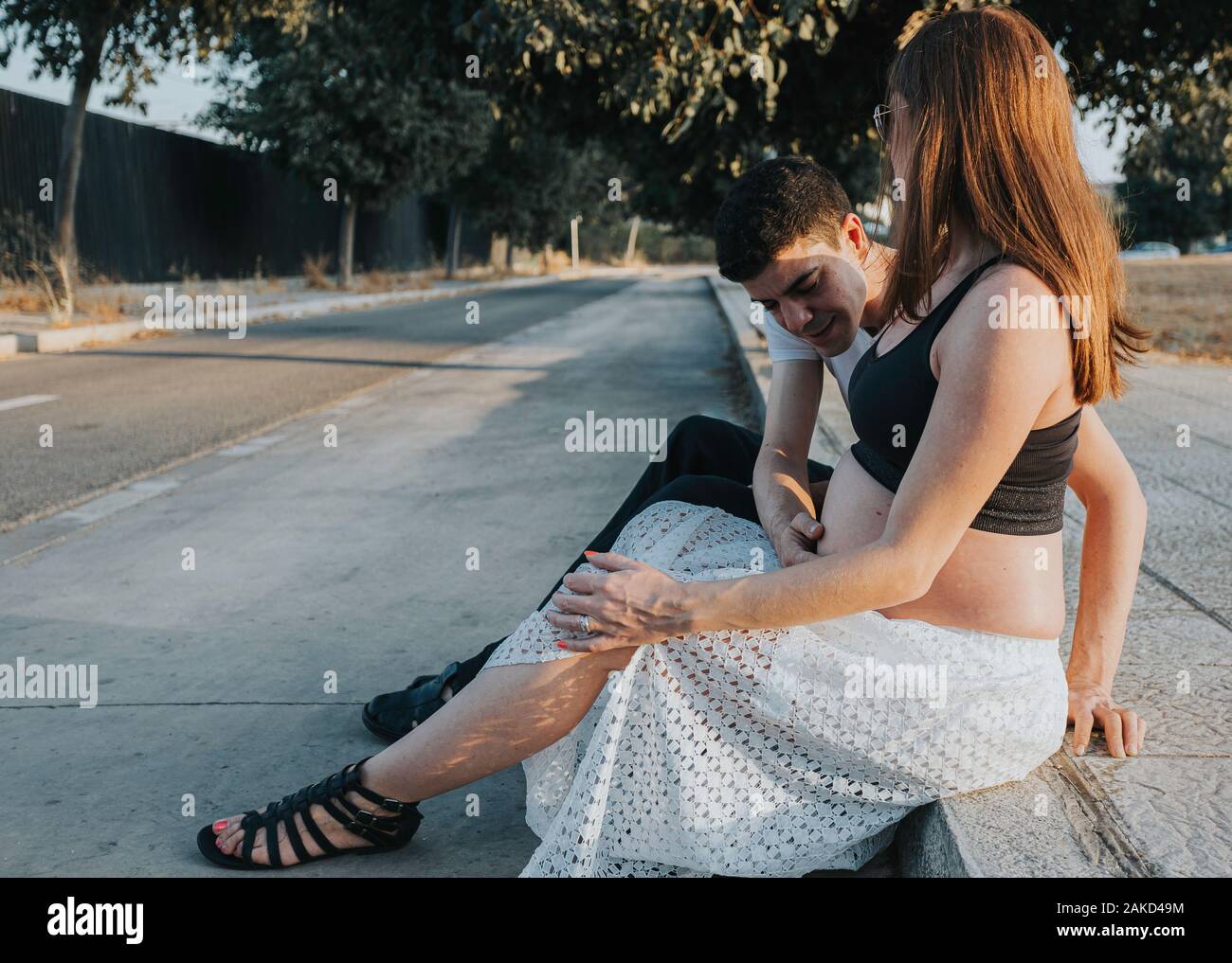 Young caucasian pregnant couple assis sur le trottoir Banque D'Images