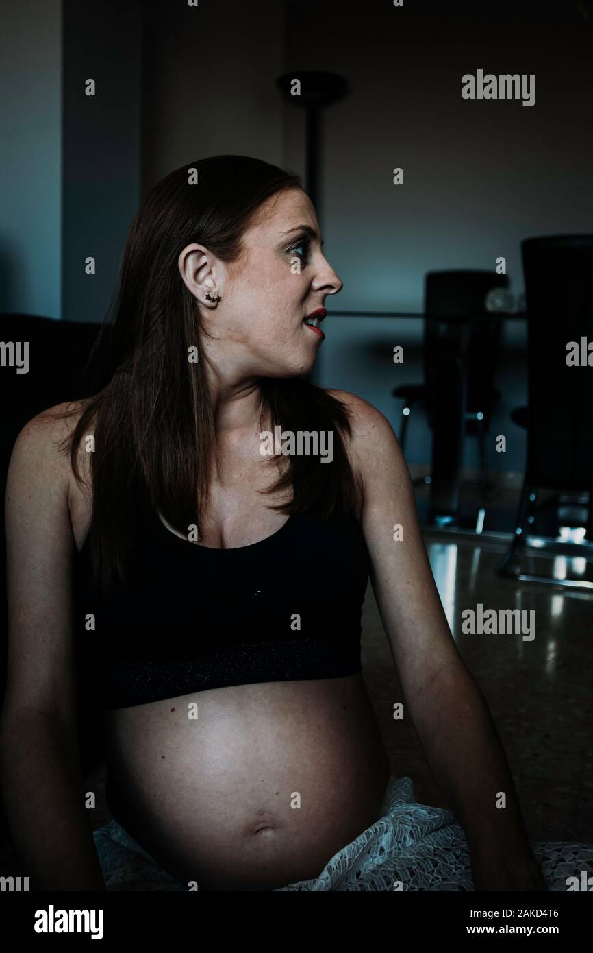 Jeune femme enceinte réfléchie dans les vêtements de sport et d'un salon à l'étage dans la chambre Banque D'Images