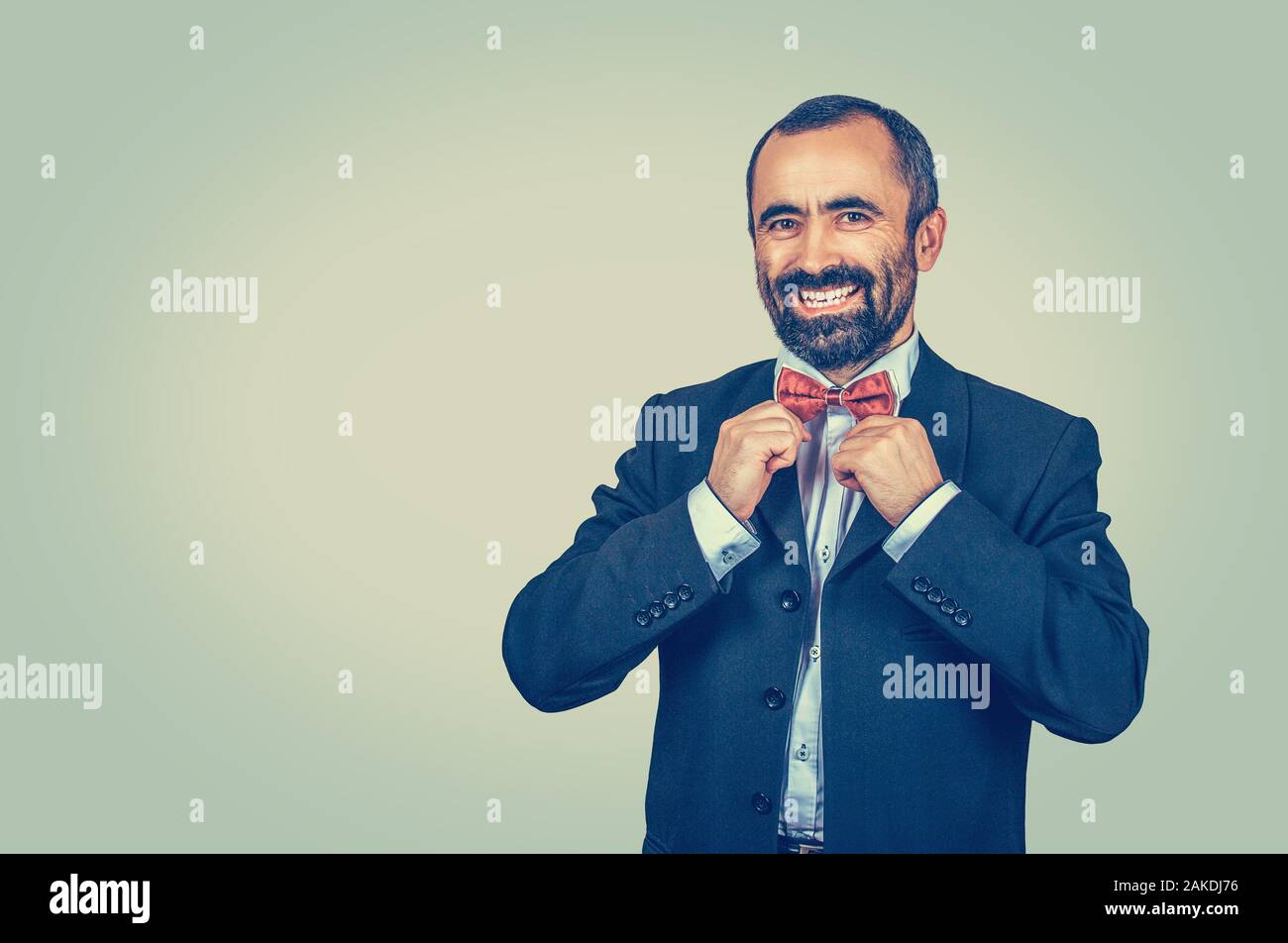 Homme barbu à bon costume foncé avec chemise bleue, réglage arc rouge. Grand sourire à la recherche d'appareil photo. L'émotion positive jaune vert lumineux. w Banque D'Images