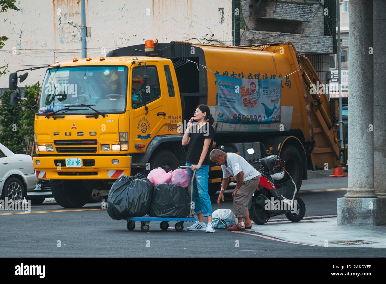 Un homme aide une femme prendre ses sacs d'ordures à une collection camion alors qu'elle parle au téléphone à Kaohsiung, Taiwan Banque D'Images