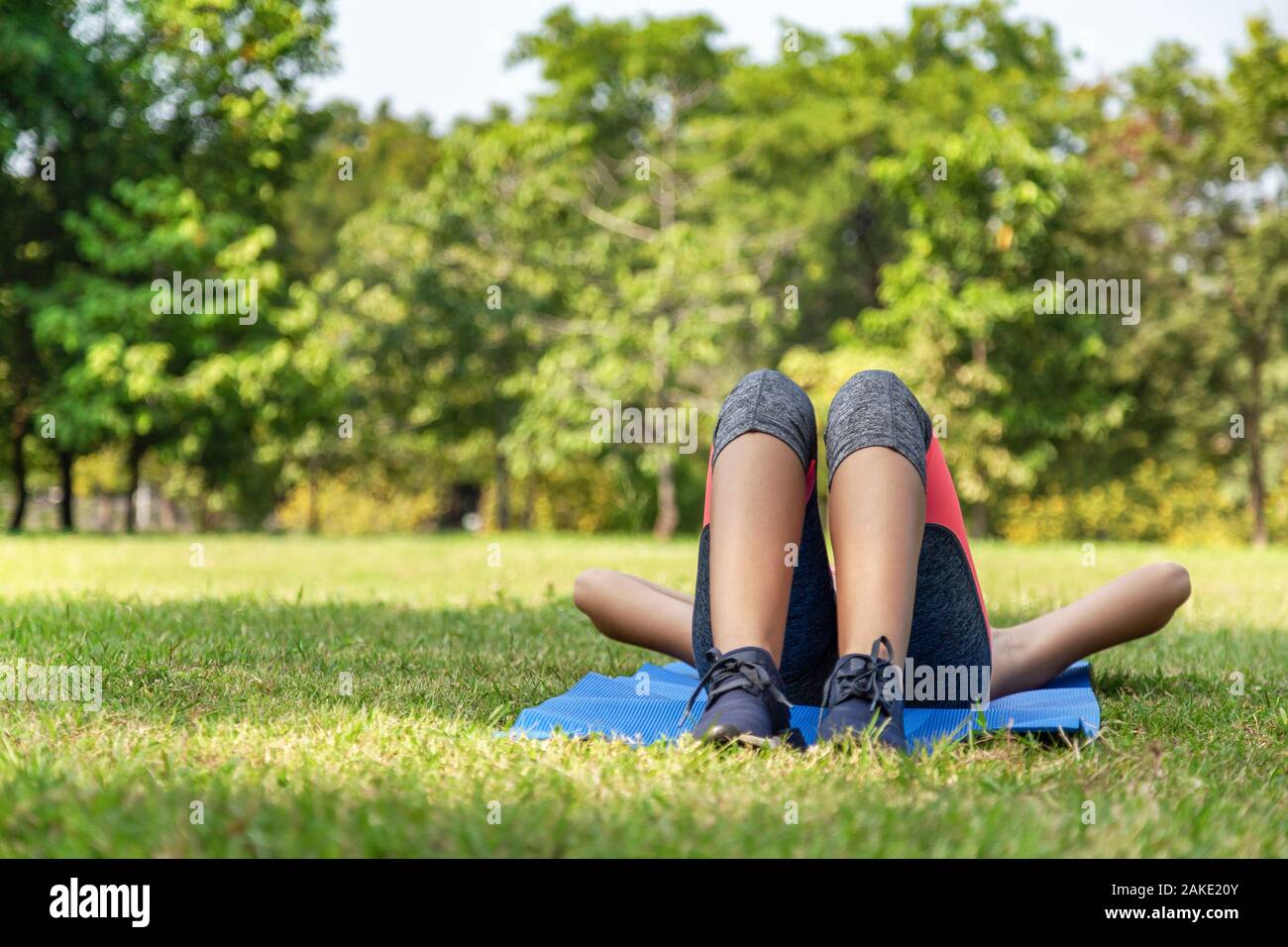 Les jeunes adolescentes dans le sport répondre à prévoir pour dormir ou se détendre sur l'herbe verte dans le parc après l'exécution de l'exercice dans matin d'été avec des sunlig Banque D'Images