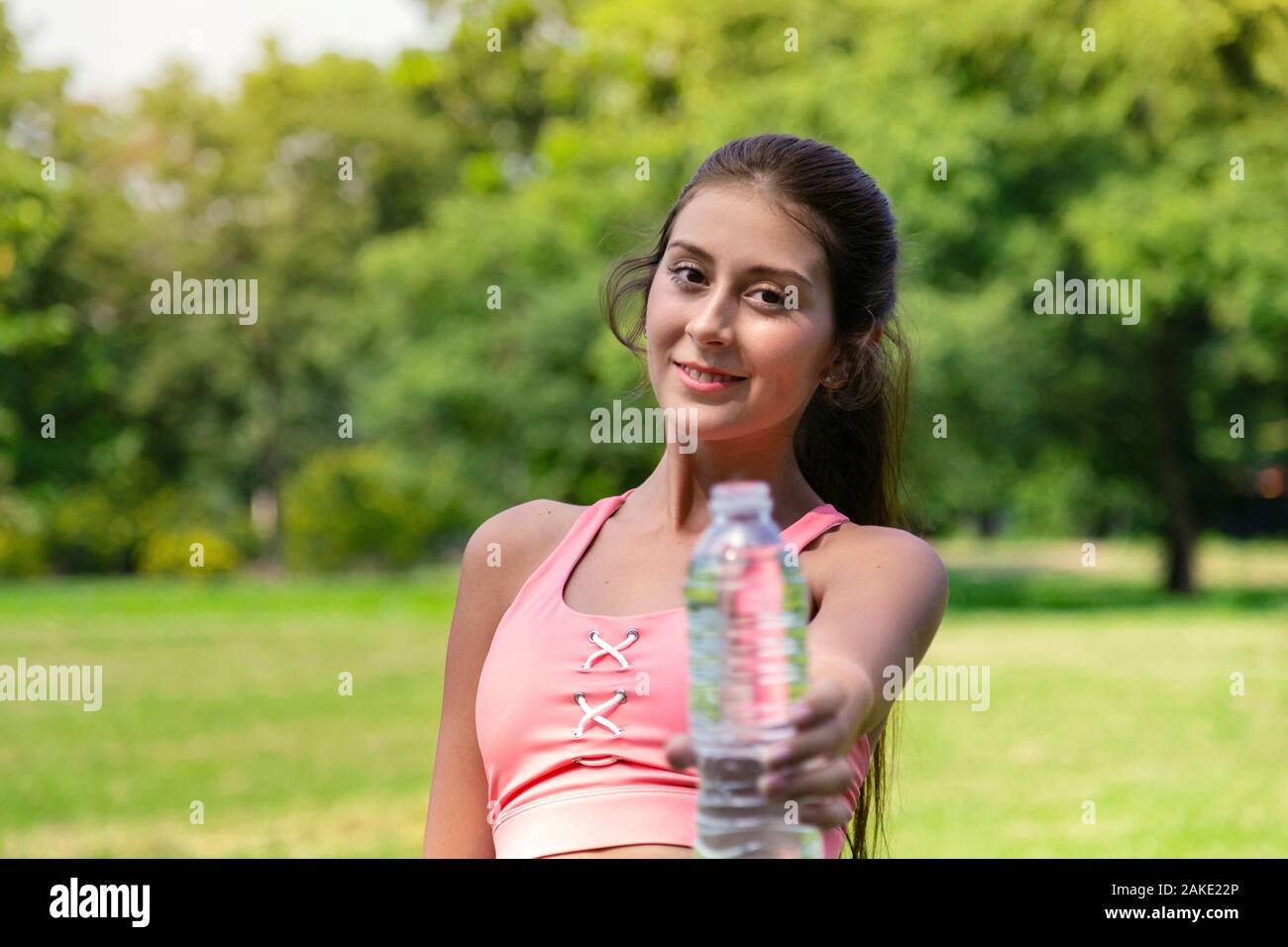 Souriante jeune adolescente dans le sport et l'eau potable à donner à un ami bouteille d'une bonne vie saine après l'exécution de l'exercice dans parc avec accueil chaleureux sunli Banque D'Images
