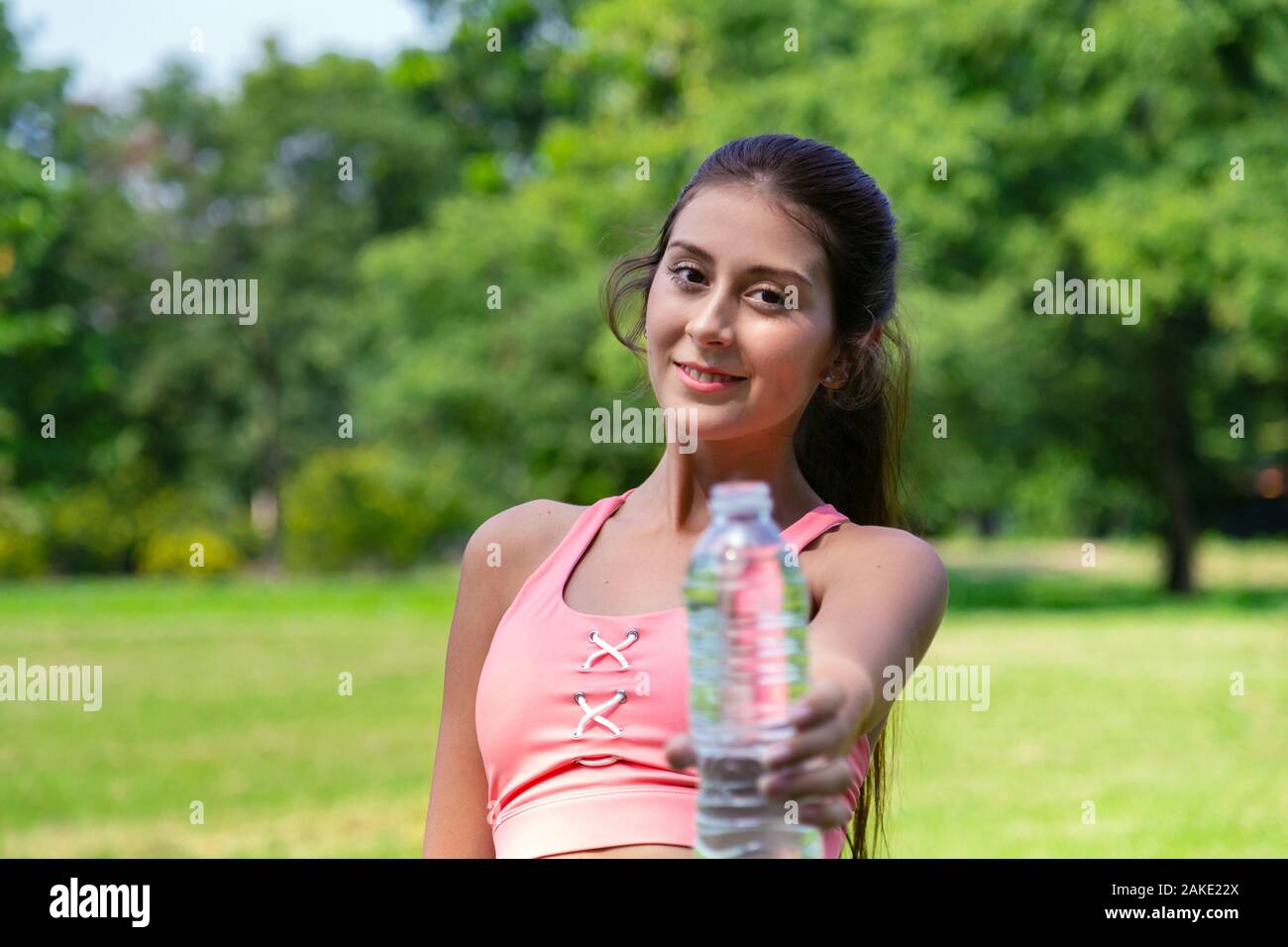 Souriante jeune adolescente dans le sport et l'eau potable à donner à un ami bouteille d'une bonne vie saine après l'exécution de l'exercice dans le parc l'été weeke Banque D'Images