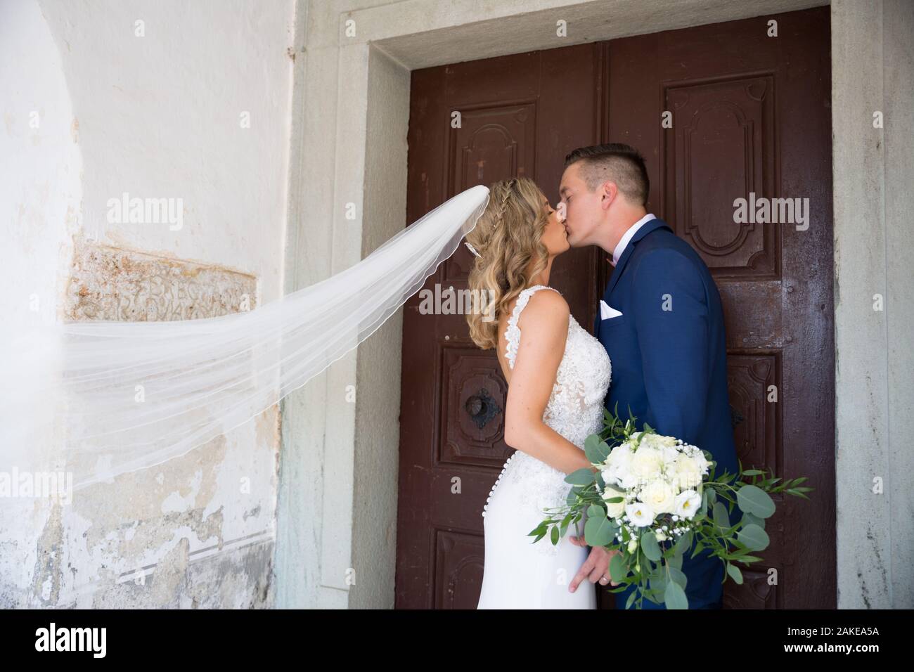 Le Baiser. Mariée et le marié embrasse tendrement en face de portail de l'église. Banque D'Images