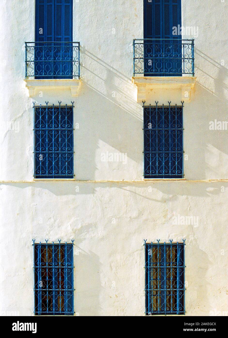 Grils métalliques ornés sur des fenêtres bleues dans un mur blanc, ombres du milieu de l'après-midi, Dit Sidi Bou, Tunisie Banque D'Images