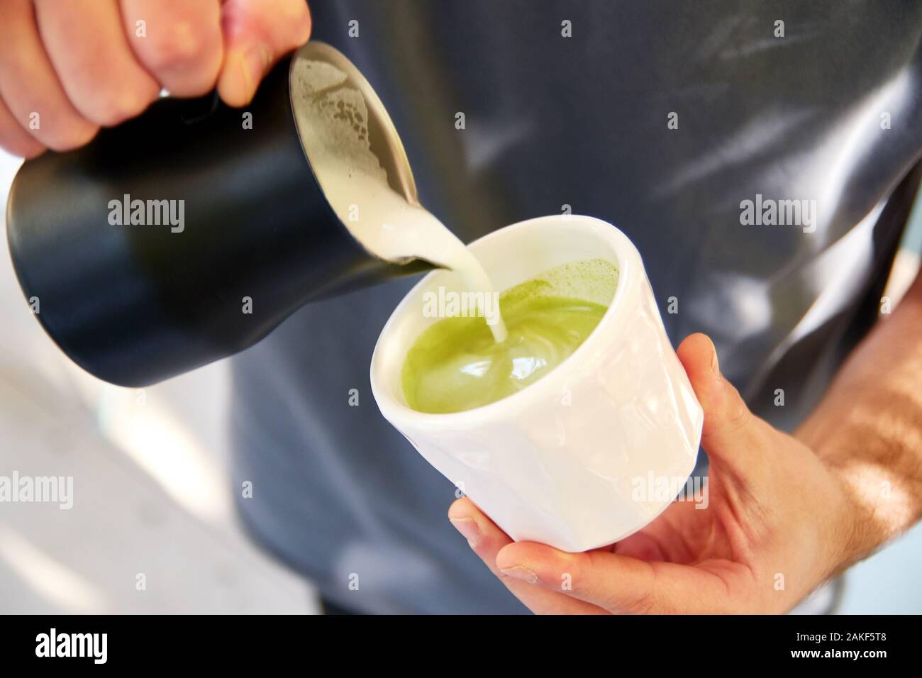 Barista mâle faisant matcha vegan cappuccino avec du lait d'avoine avec latte art in outdoor cafe. Banque D'Images