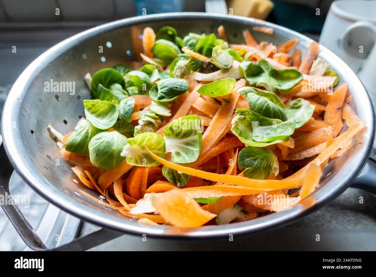 Graines et de pelures de légumes carotte dans une passoire métallique dans une cuisine dans le cadre de la préparation d'un repas. Banque D'Images