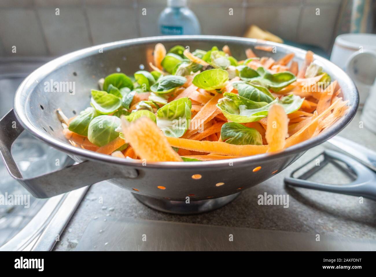 Graines et de pelures de légumes carotte dans une passoire métallique dans une cuisine dans le cadre de la préparation d'un repas. Banque D'Images