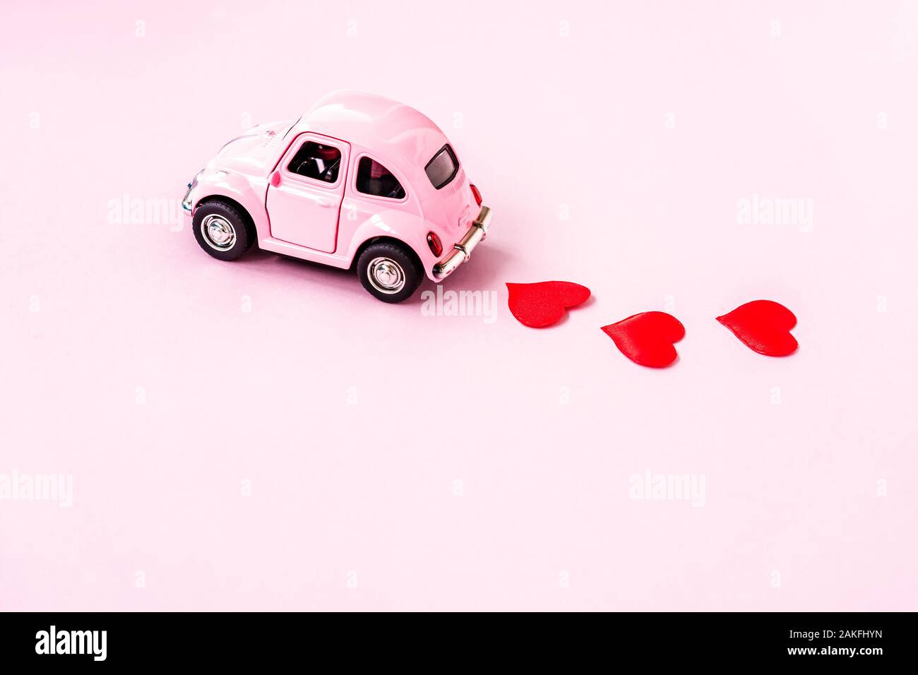 Sotchi, Russie - 8 janvier, 2020 : Rose retro toy voiture rouge pour la Saint-Valentin sur fond rose avec coeur confettis. 14 février, 8 mars, Journée internationale de la femme heureuse. Banque D'Images