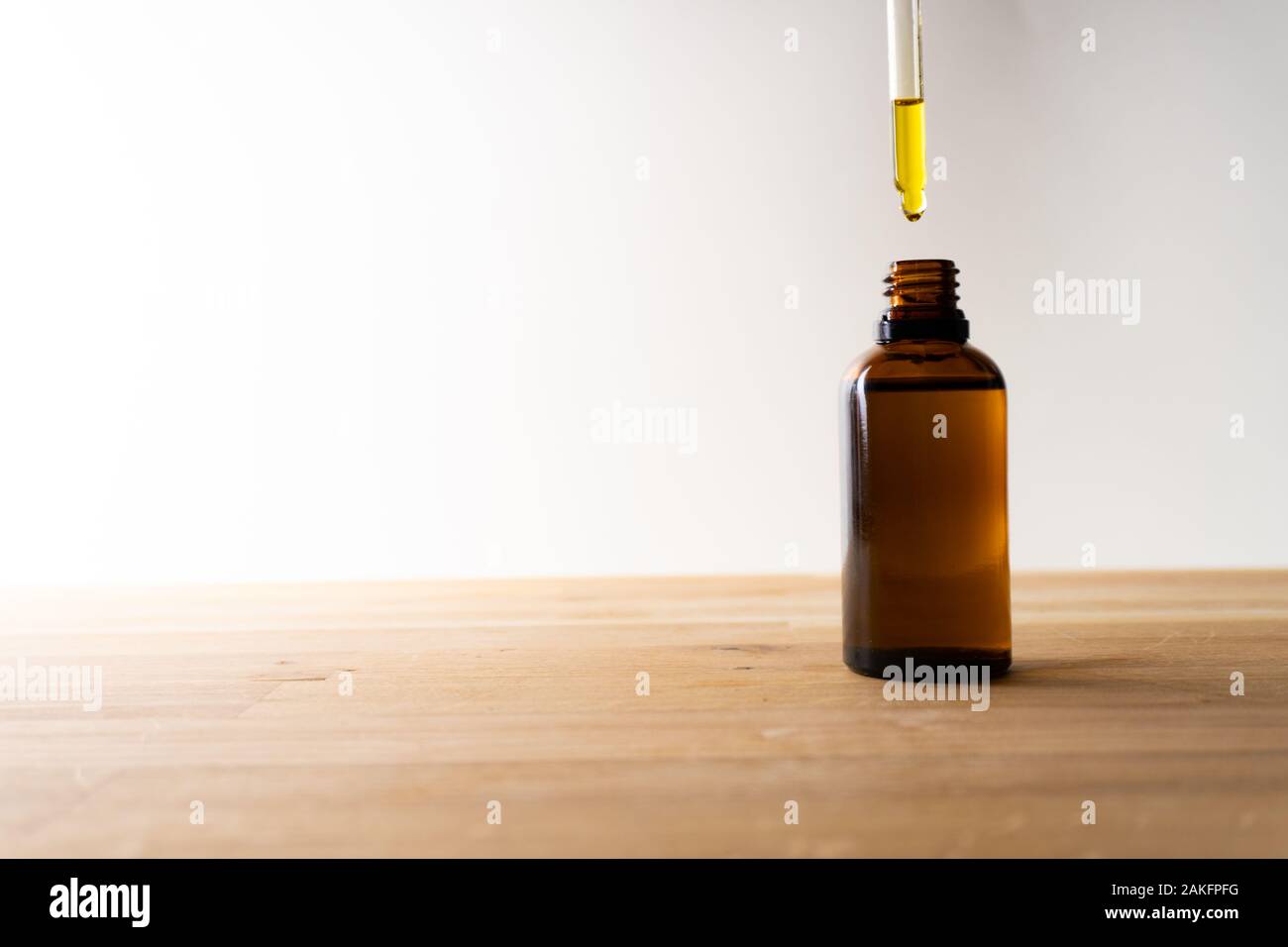 L'huile de la CDB ou toute autre huile de les faire tomber dans une petite bouteille debout sur une planche en bois - Fond blanc Banque D'Images