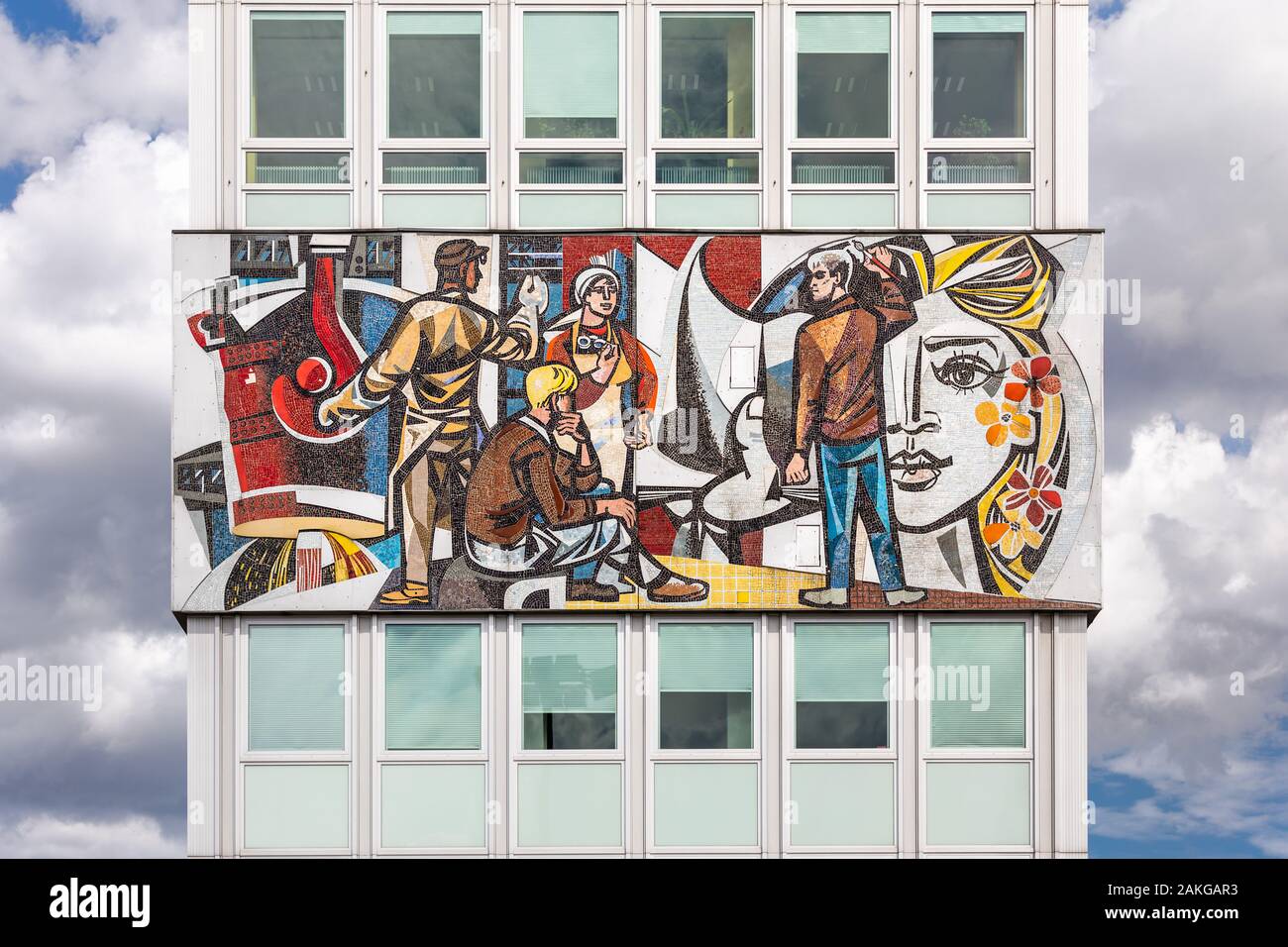 Gros plan symétrique d'une mosaïque soviétique colorée sur une façade en hauteur, représentant les ouvriers, contre un ciel bleu d'été avec des nuages puffy Banque D'Images