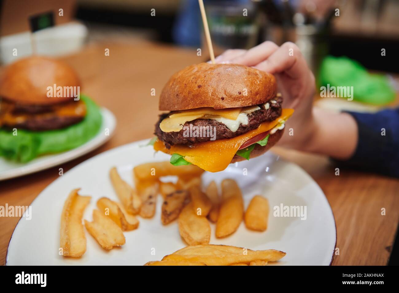 Cheeseburger juteux dans la main des filles. Hamburger de bœuf naturel avec double fromage servi avec des pommes de terre. Dîner à haute teneur en calories dans le café. Banque D'Images