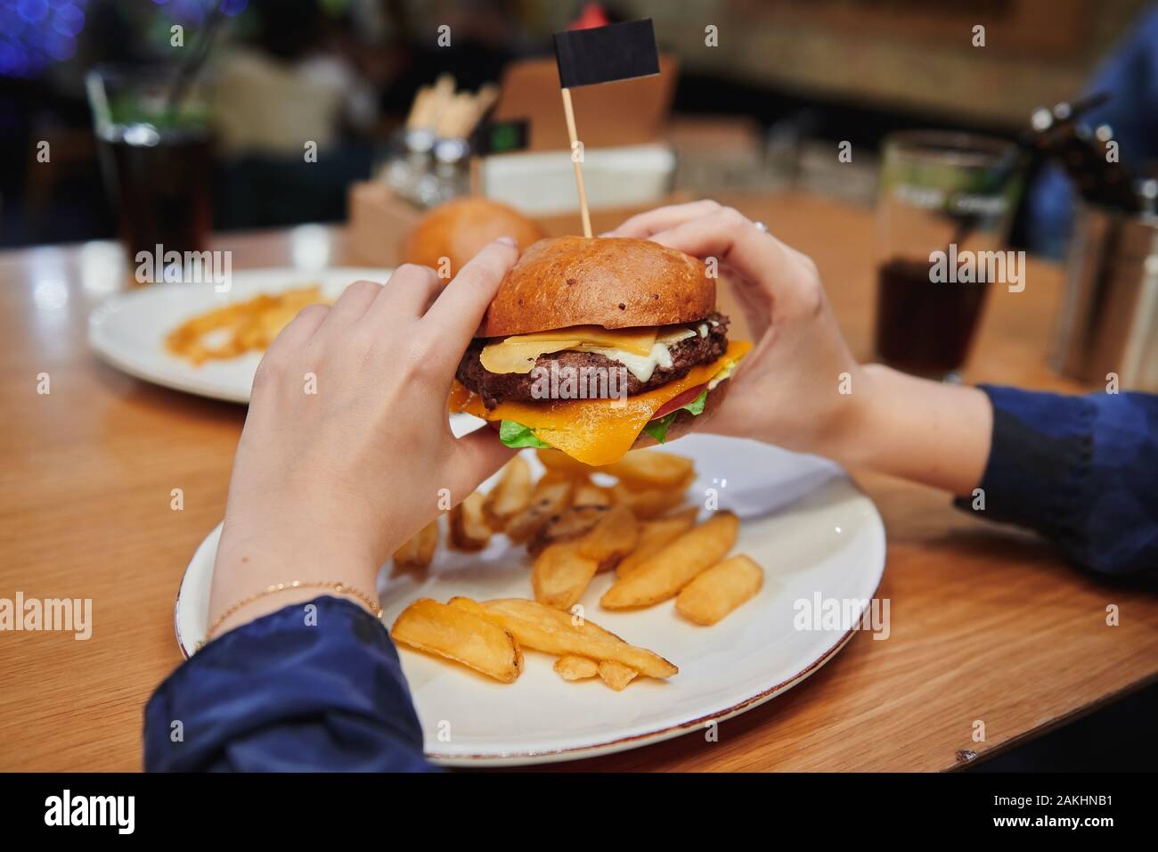 Cheeseburger juteux dans les mains des filles. Hamburger de bœuf naturel avec double fromage servi avec des pommes de terre. Dîner à haute teneur en calories dans le café. Banque D'Images