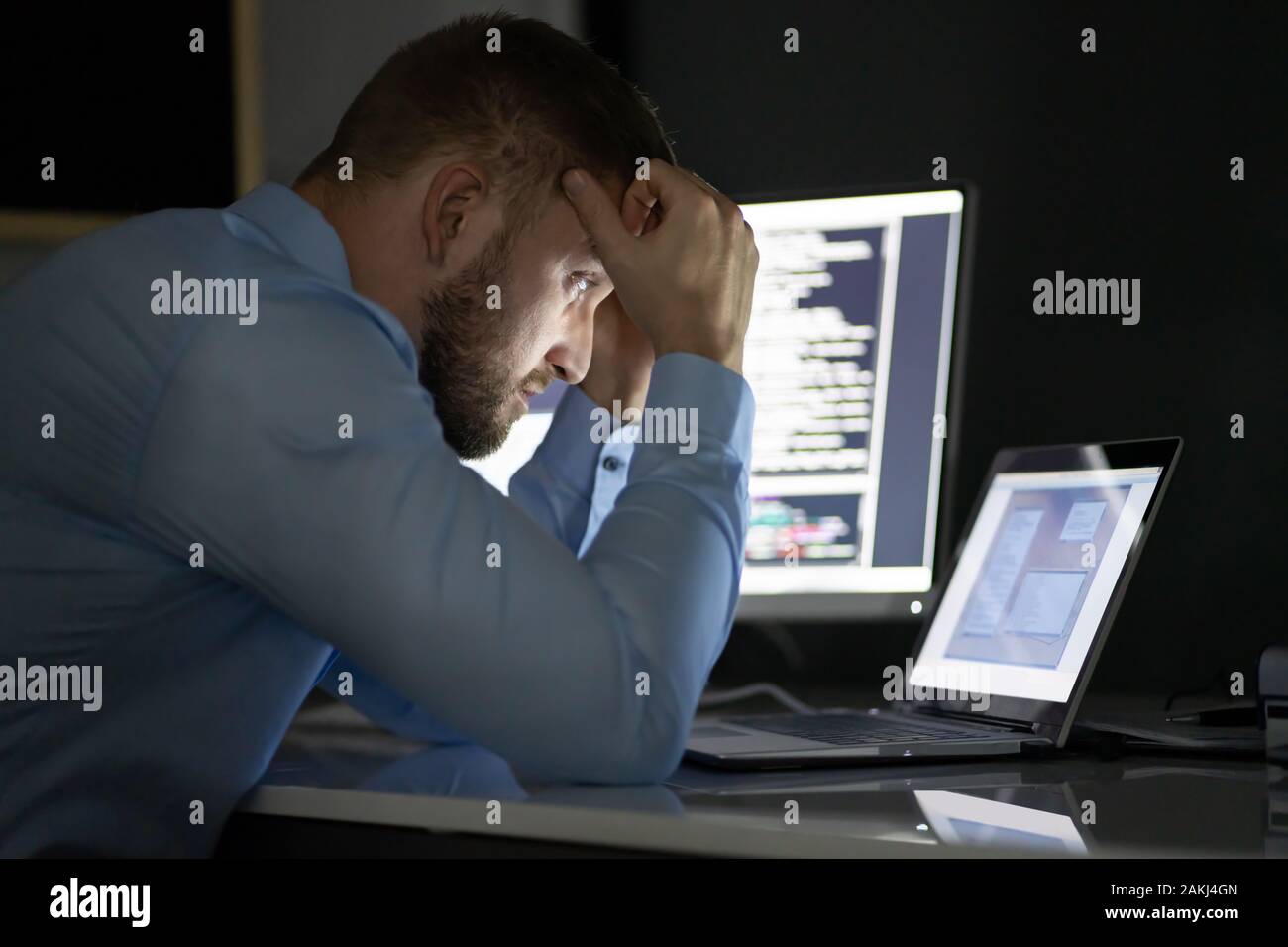 Programmeur inquiète travaillant tard dans la nuit sur plusieurs écrans d'ordinateur Banque D'Images